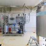 High-tech industrial machinery inside a modern factory. Pipes and equipment dominate the space.